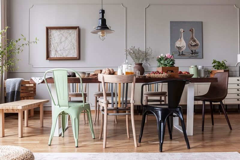 A dining room featuring an eclectic mix of chairs around a rustic wooden table, with pendant lighting