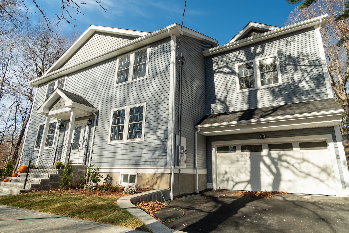 A remodeled two-story house featuring a garage and driveway, highlighting contemporary design and attractive landscaping.