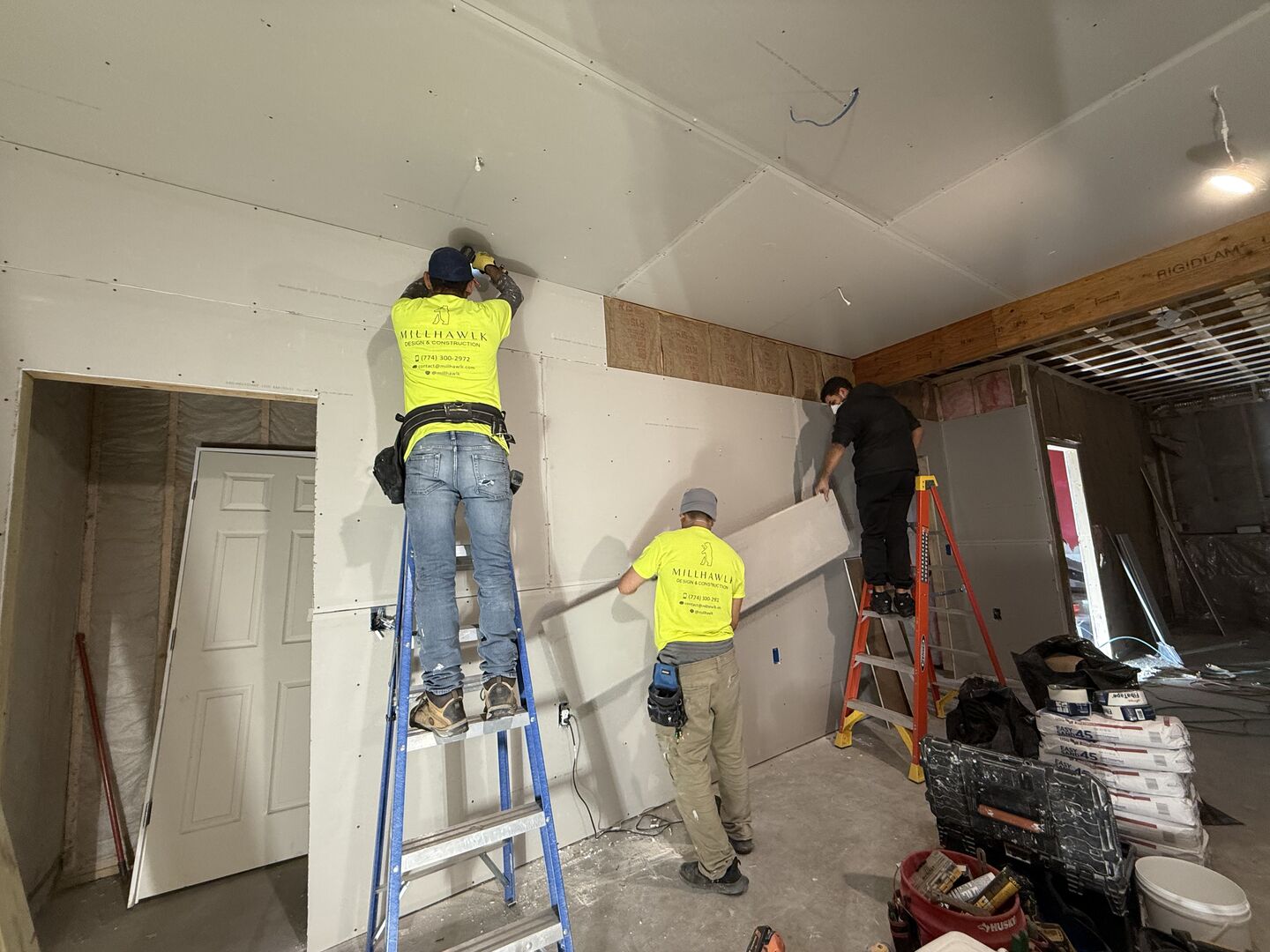 Three contractors standing on ladders while they hanging up drywall.